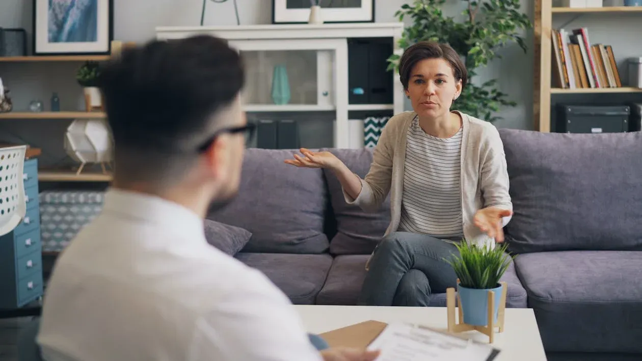 A woman sat on a sofa, talking to a man sat just in front of the camera