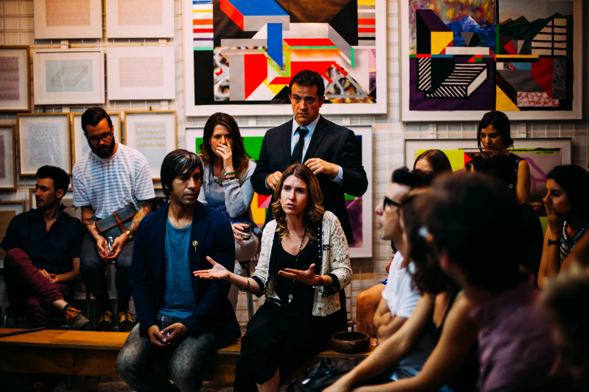 A group of people discussing something, with a number of pieces of art on the wall
behind them