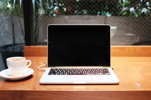 A latop on a wooden desk with a mug of coffee on the left