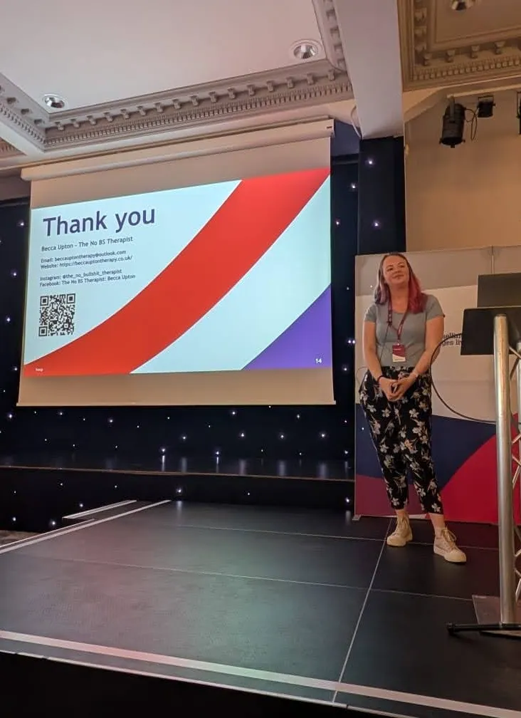 Becca Giving a BACP talk, standing off to the right near a podium, with a "thank you" presentation slide on the left